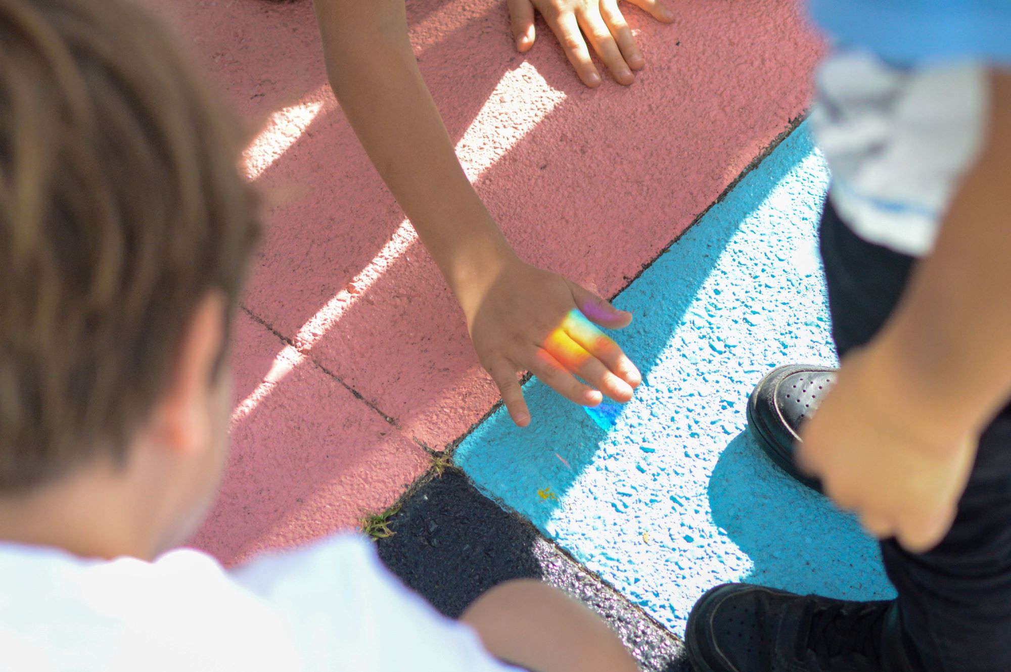 Des enfants utilisent un prisme et font apparaître un arc-en-ciel sur le sol